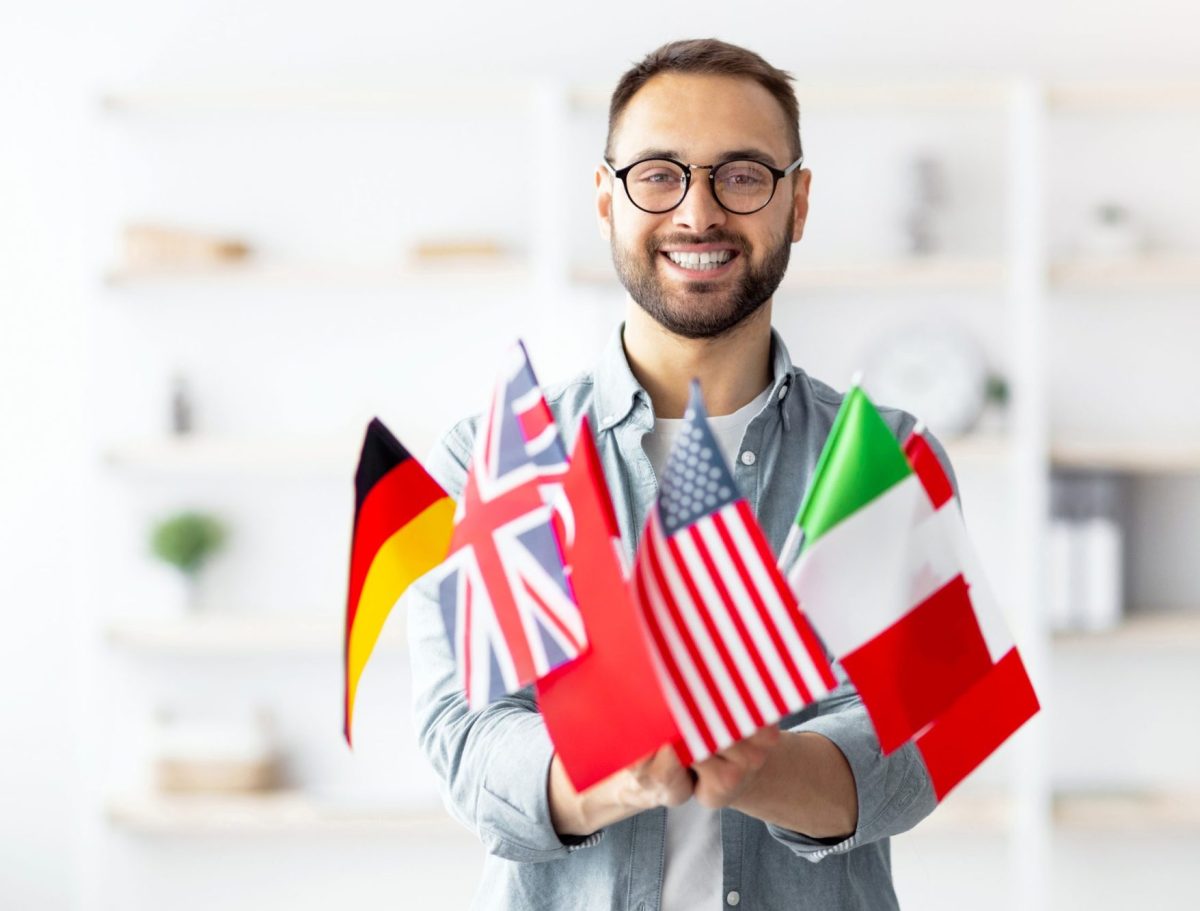 Modern education and student exchange. Cheerful young Caucasian guy holding bunch of different flags at home
